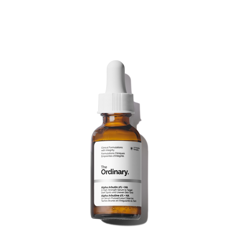 A bottle of The Ordinary Alpha Arbutin 2% + HA serum in amber glass with a white dropper cap, labeled as a high-strength formula targeting dark spots and uneven skin tone